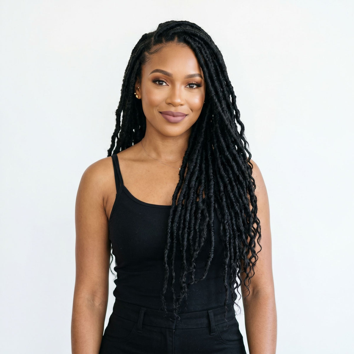Model in a black tank top wearing long natural black locs styled from bulk braiding hair extensions against a plain white wall