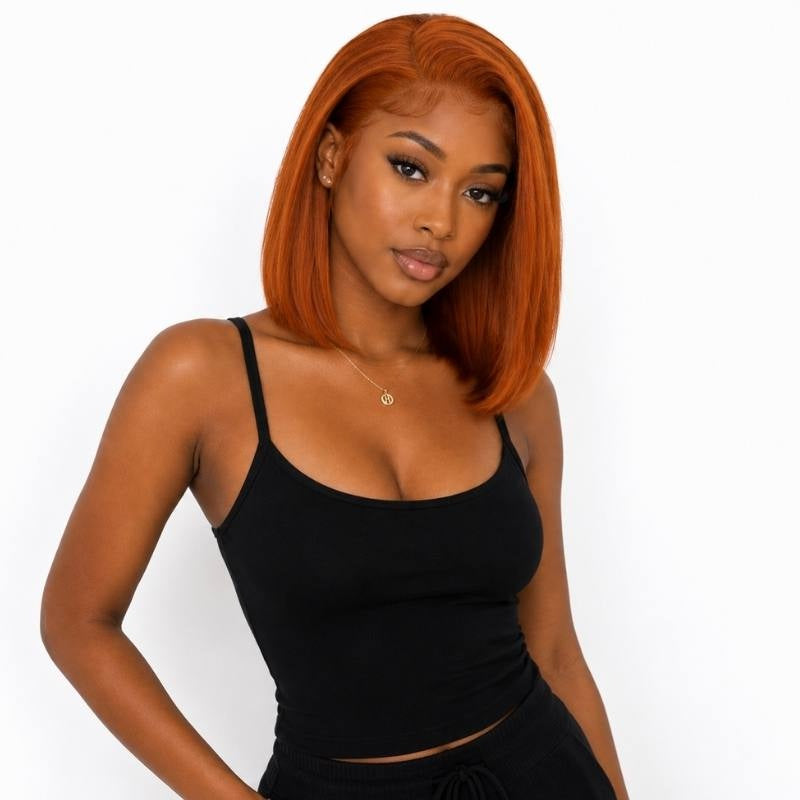 Half body shot of a model in a black tank wearing a straight cinnamon orange ginger bob human hair wig parted off centre