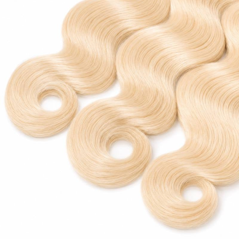 Close-up of the ends of three bundles of blonde body wave sew-in hair extensions curling into rings on a white background
