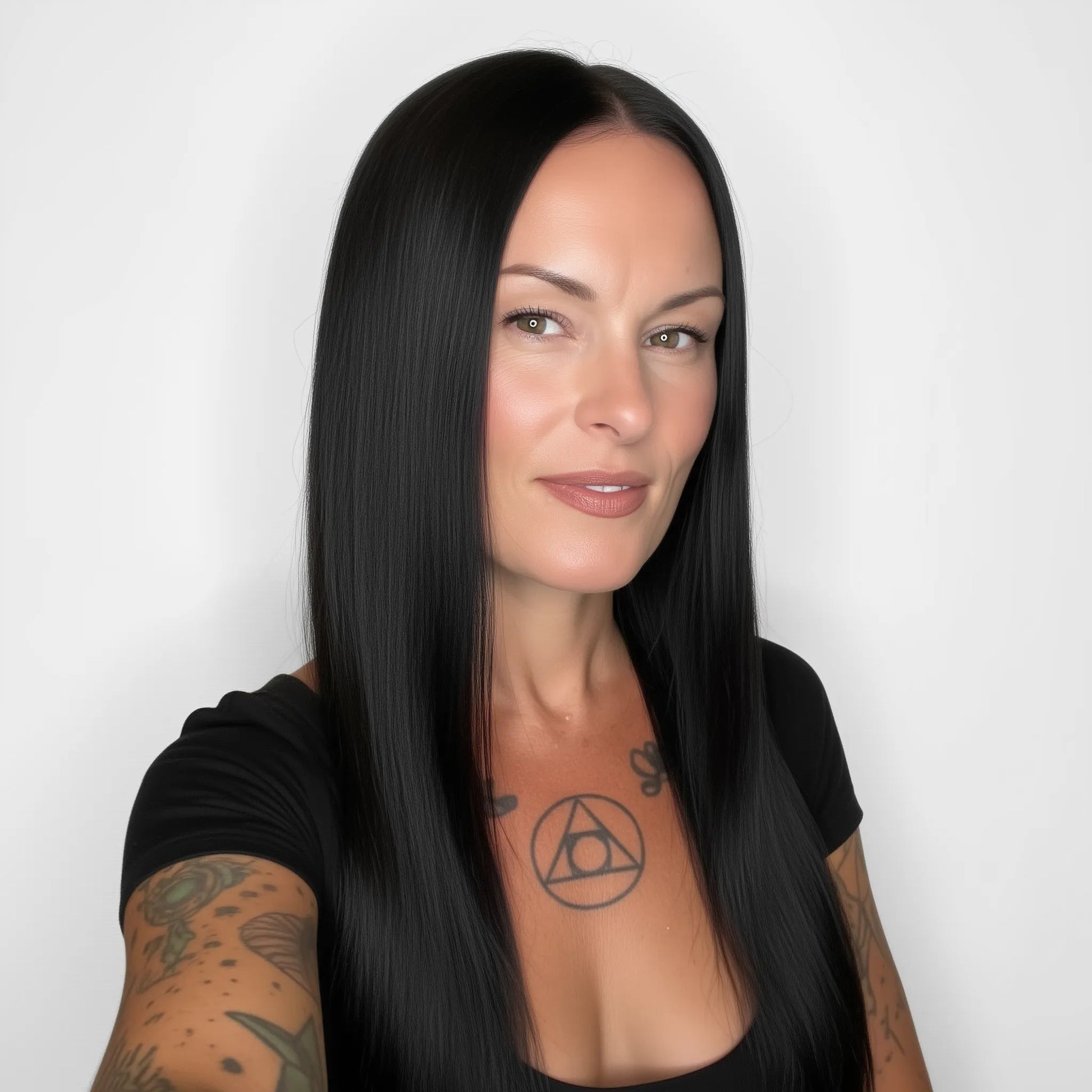 Woman with long black hair and tattoos on arms against a white background