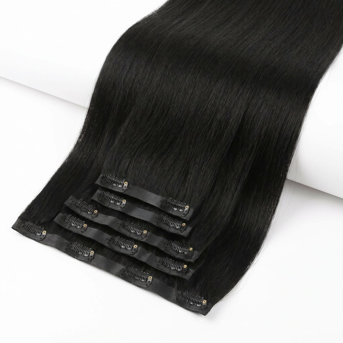 Jet black straight clip-in hair extensions fanned at an angle so the clips on every seamless weft in the set are visible