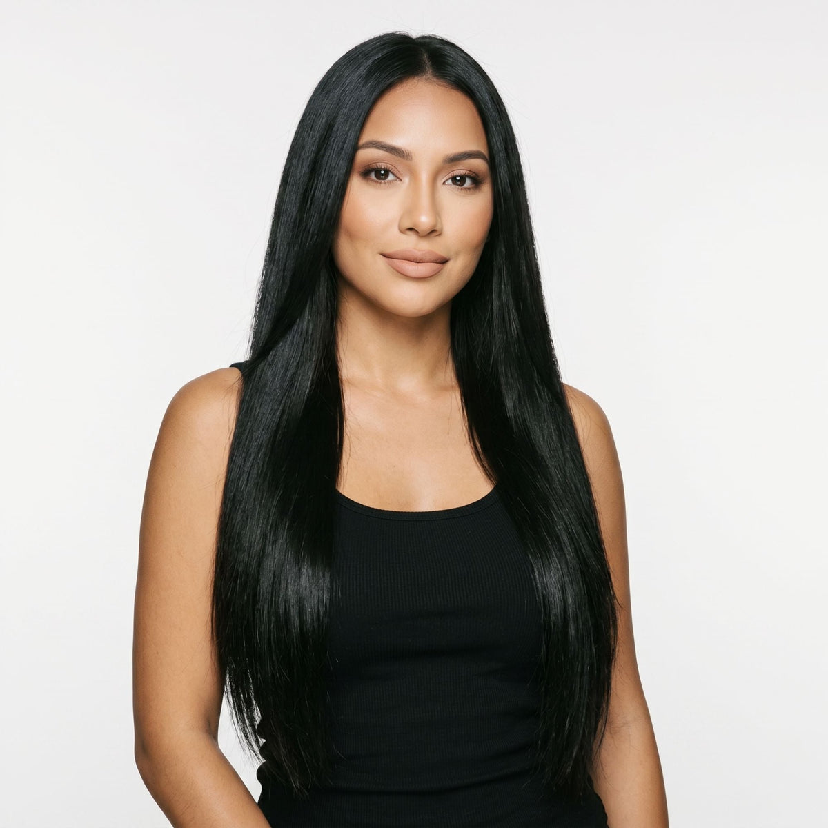 Model facing forward wearing long straight jet black clip-in hair extensions parted in the centre against a white studio backdrop