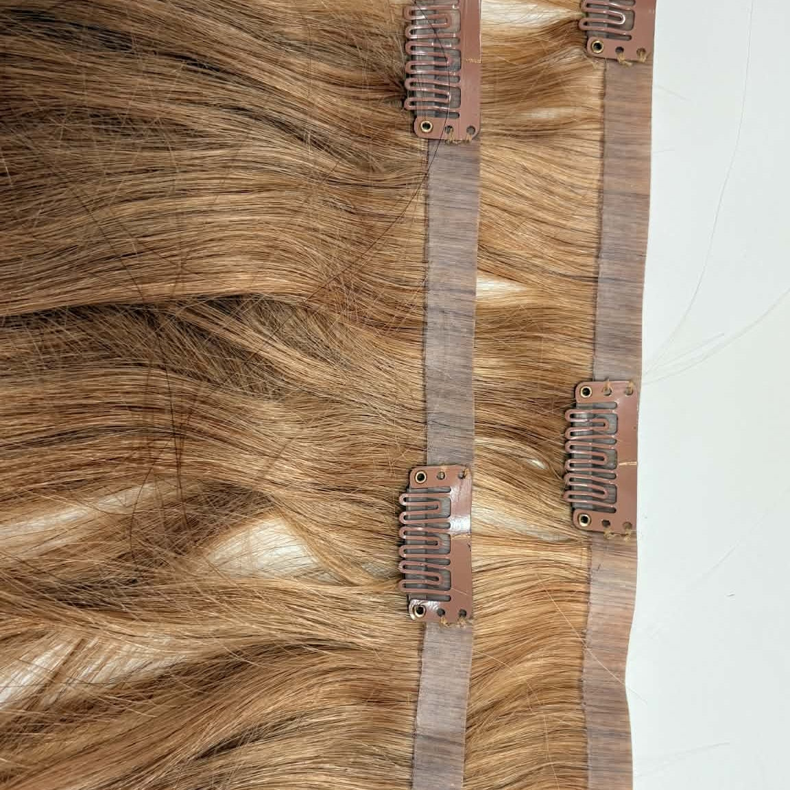 Detail view of snap clip weft strips on 20 inch honey blonde seamless clip-in hair extensions showing clip mechanism