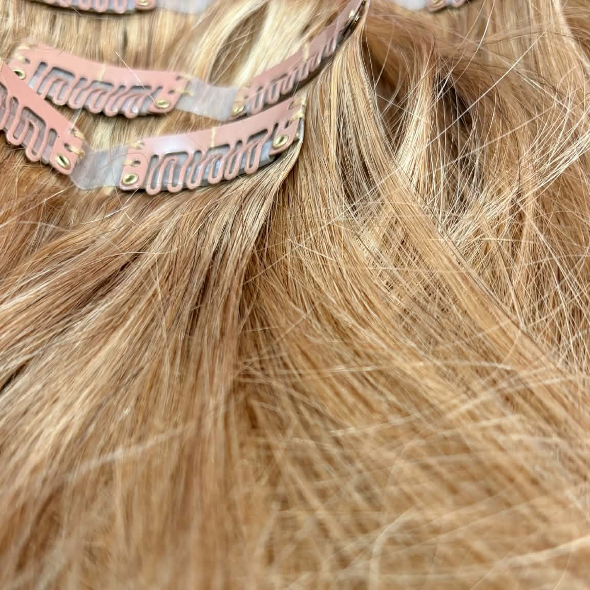 Close-up of snap clips on 20 inch honey blonde seamless clip-in hair extensions showing clip detail and straight hair texture