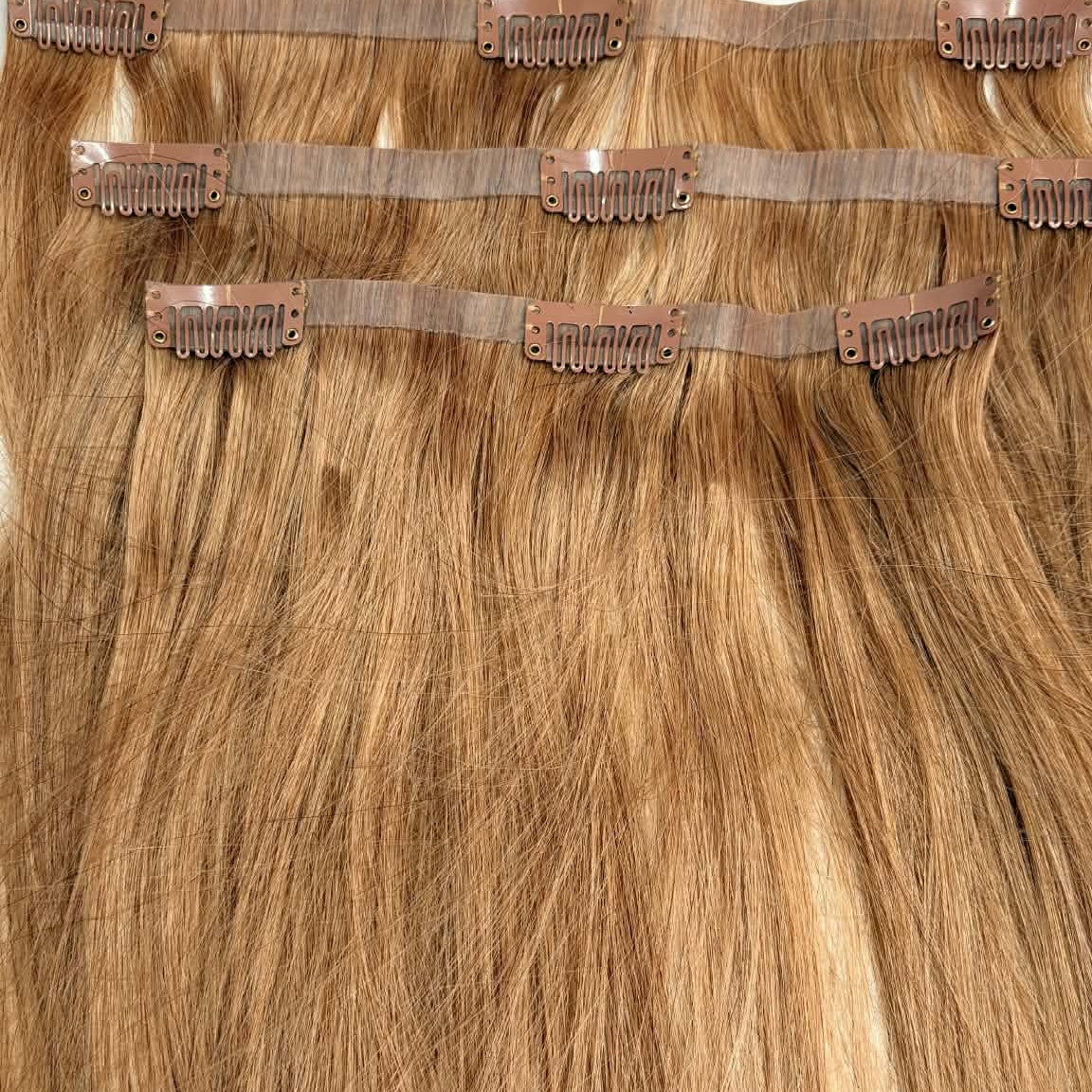 Detail of 20 inch honey blonde seamless clip-in hair extensions showing clip attachment and straight hair falling from weft
