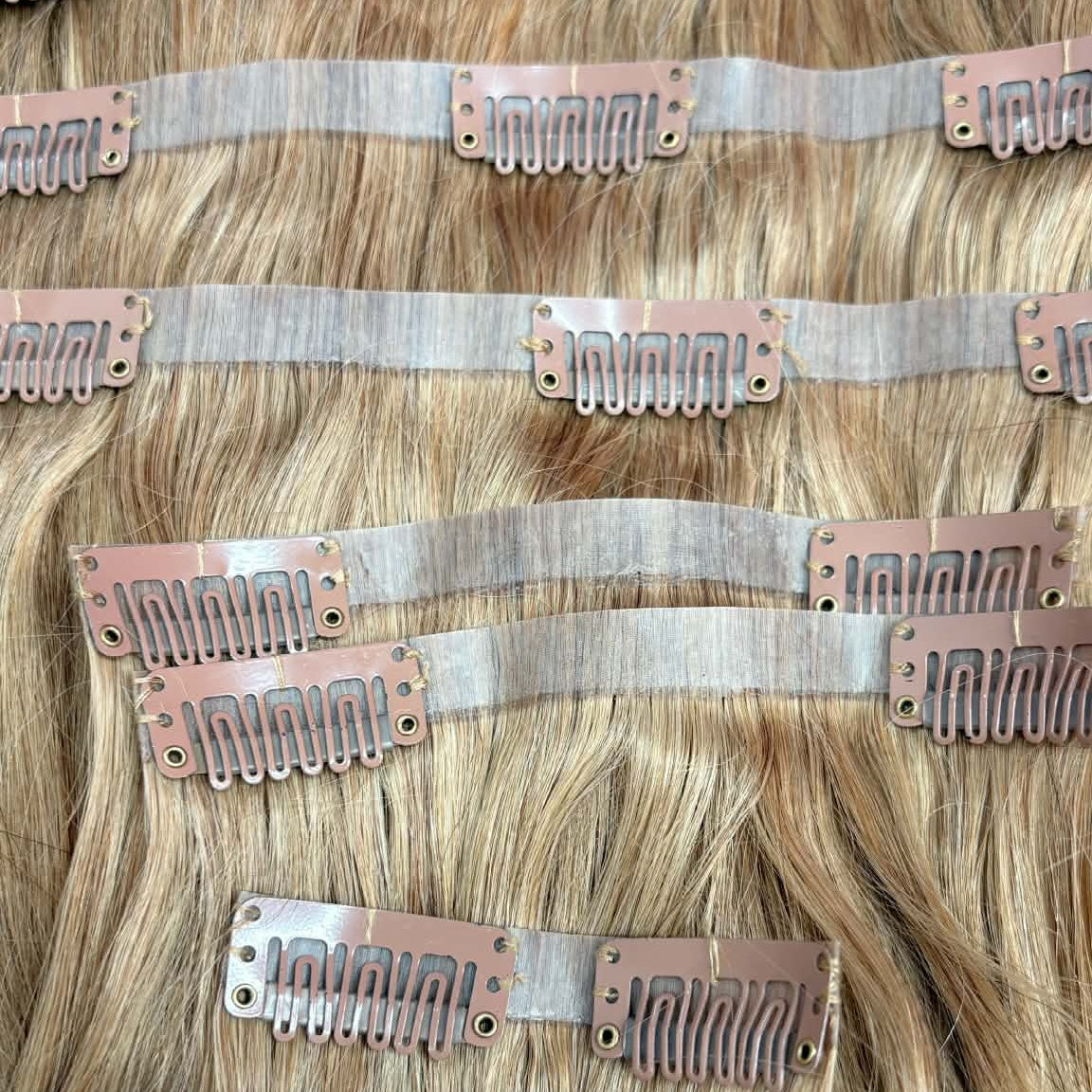 Full set of 20 inch honey blonde 27 seamless clip-in hair extensions showing snap clips on multiple weft strips