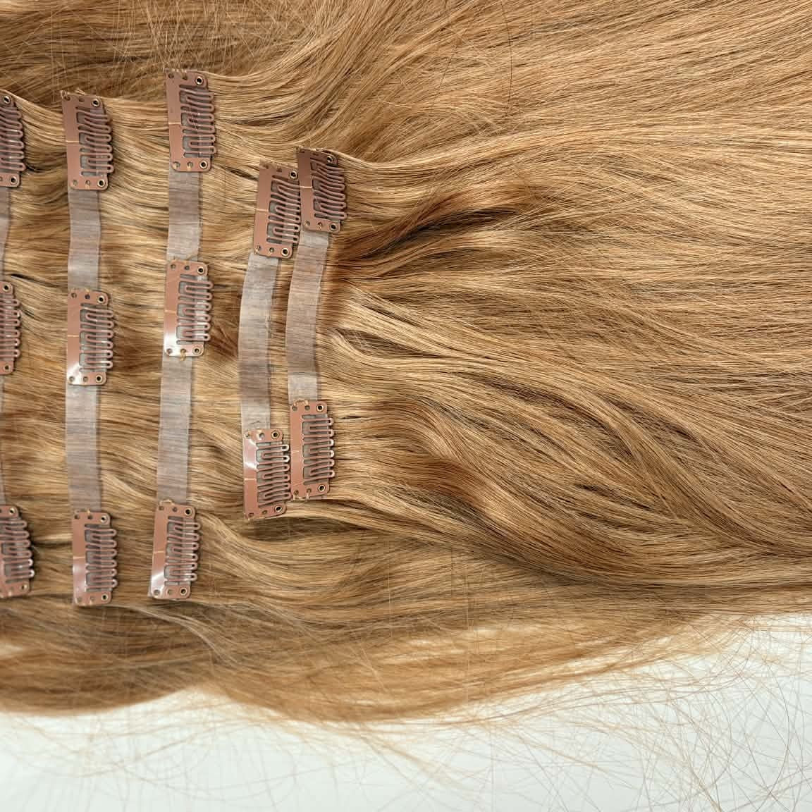 Close-up of 20 inch honey blonde seamless clip-in hair extensions weft showing multiple snap clips attached to thin weft band