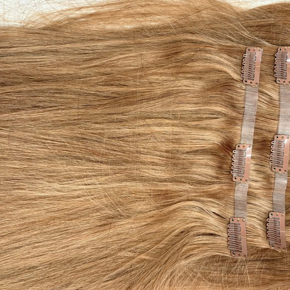 Flat lay of 20 inch honey blonde 27 seamless clip-in hair extension wefts showing clips and straight hair spread