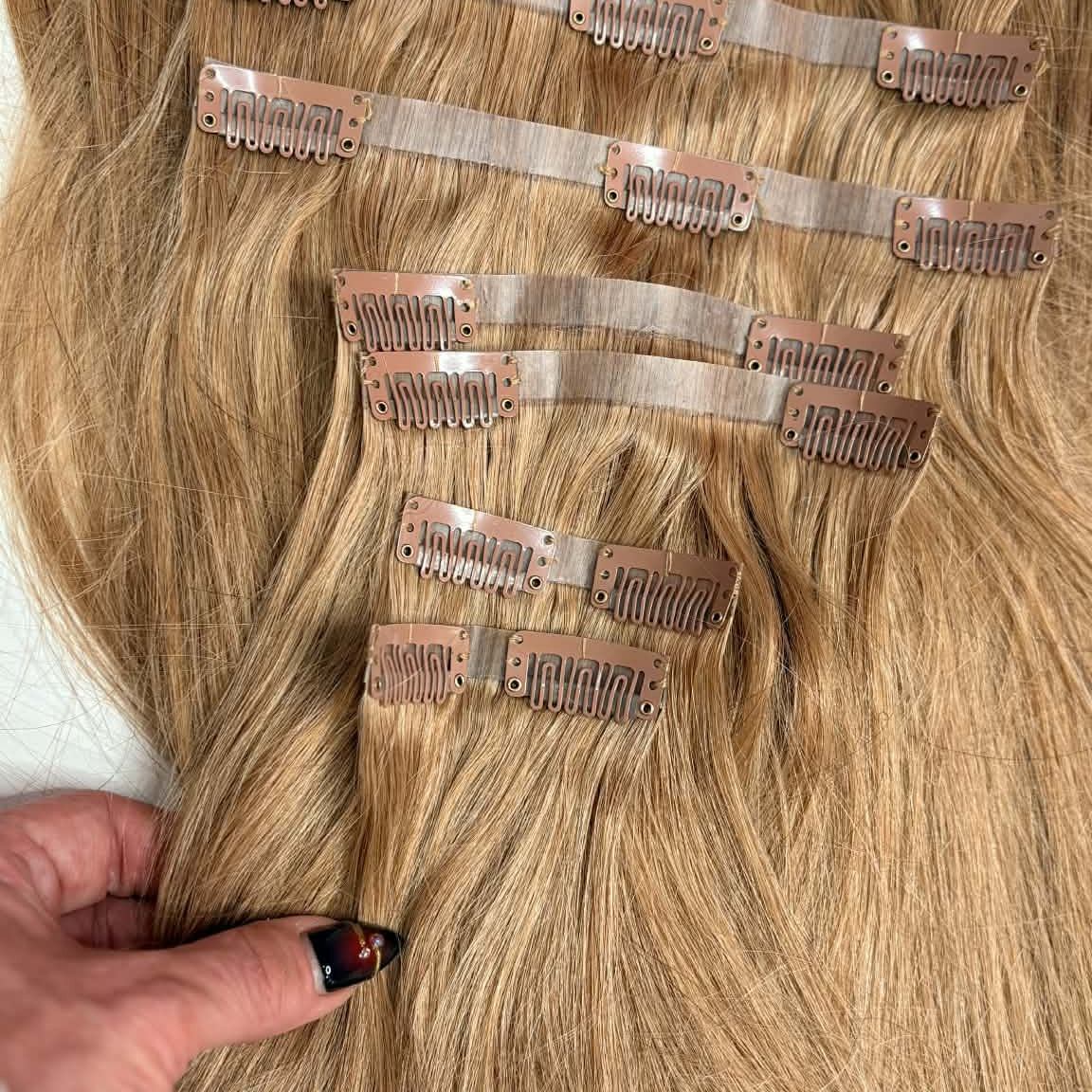 Close-up of 20 inch honey blonde seamless clip-in hair extensions weft strips showing snap clip mechanism and straight hair texture