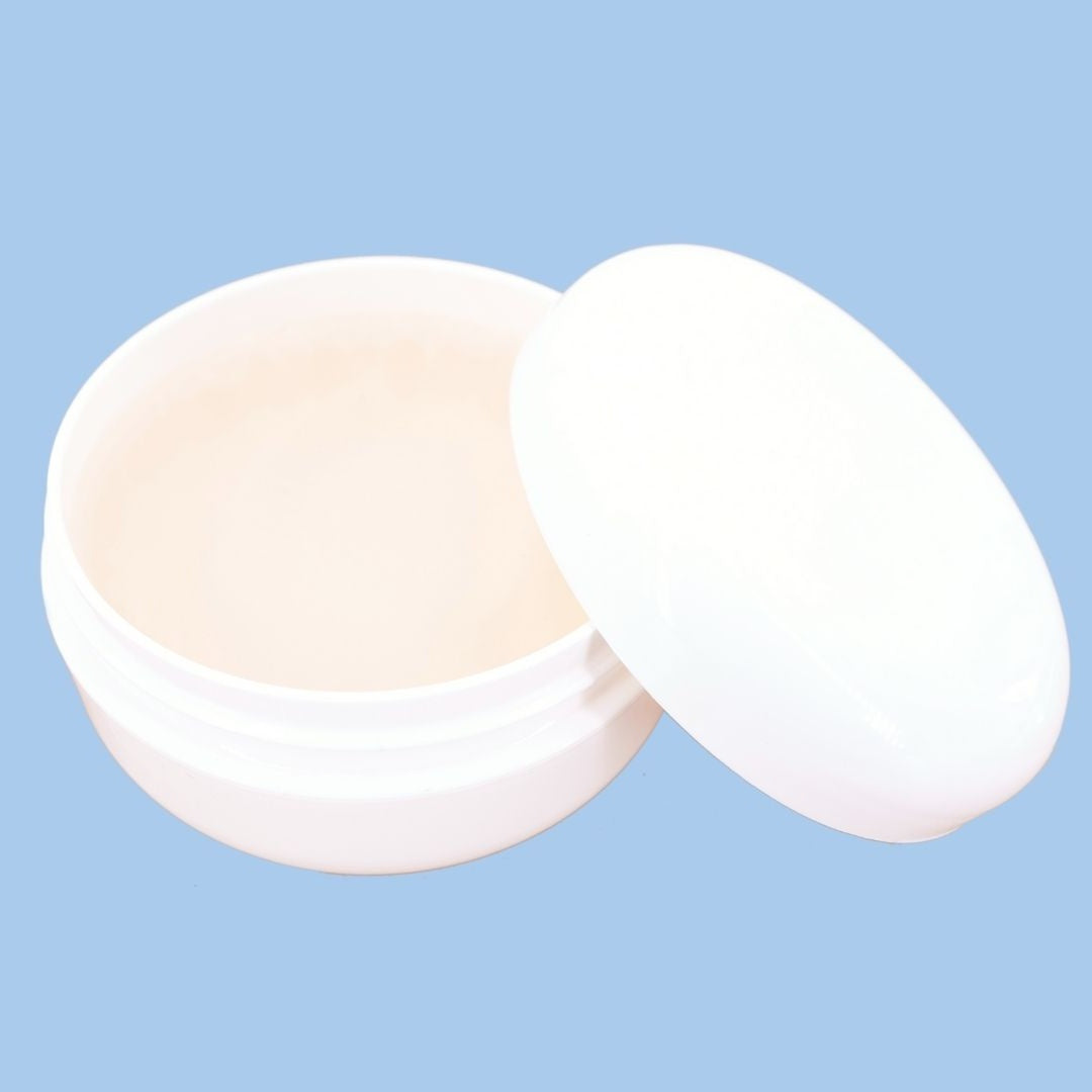 Angled view of an open edge control jar with the lid propped against it on a blue backdrop, a styling gel used with hair extensions