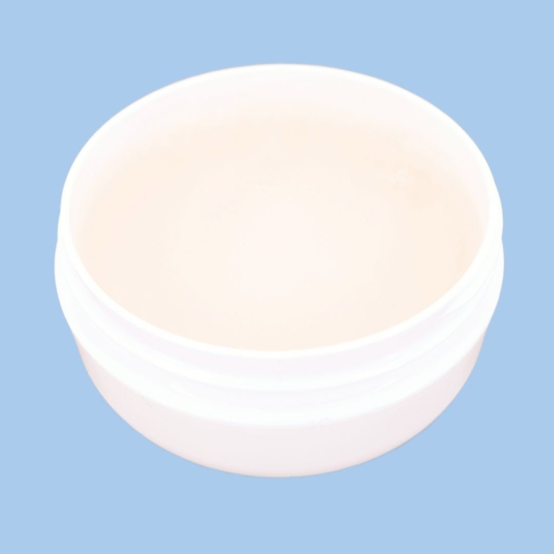 Overhead view of an open edge control jar on a blue backdrop showing the smooth cream gel used with hair extensions
