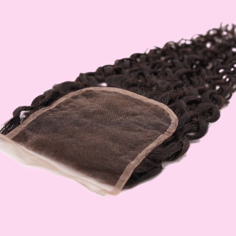 Transparent lace closure turned over on a pink backdrop to show the lace base with natural black curly hair extensions running from it