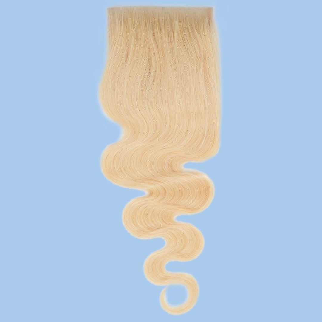 Blonde body wave hair extensions on a transparent lace closure hanging against a blue backdrop with the wave curling at the ends