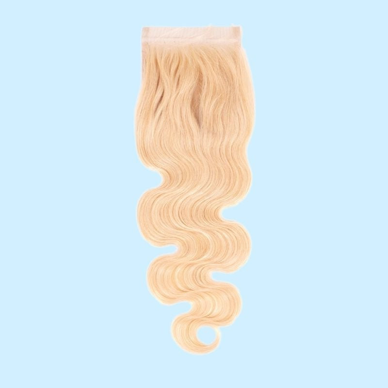 Blonde body wave hair extensions on a transparent lace closure shown against a pale blue backdrop with the wave running to the ends