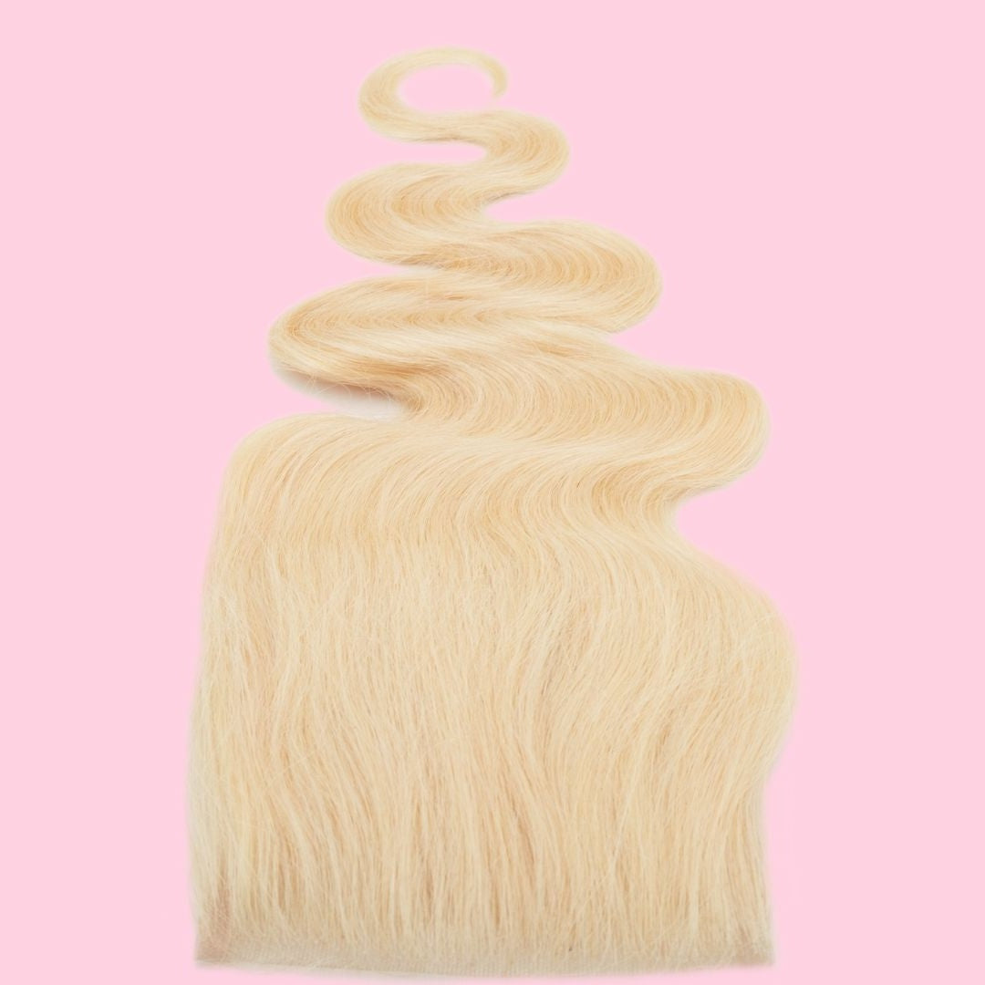 Blonde body wave hair extensions with the ends fanned wide and a wave curling above, photographed on a pink backdrop