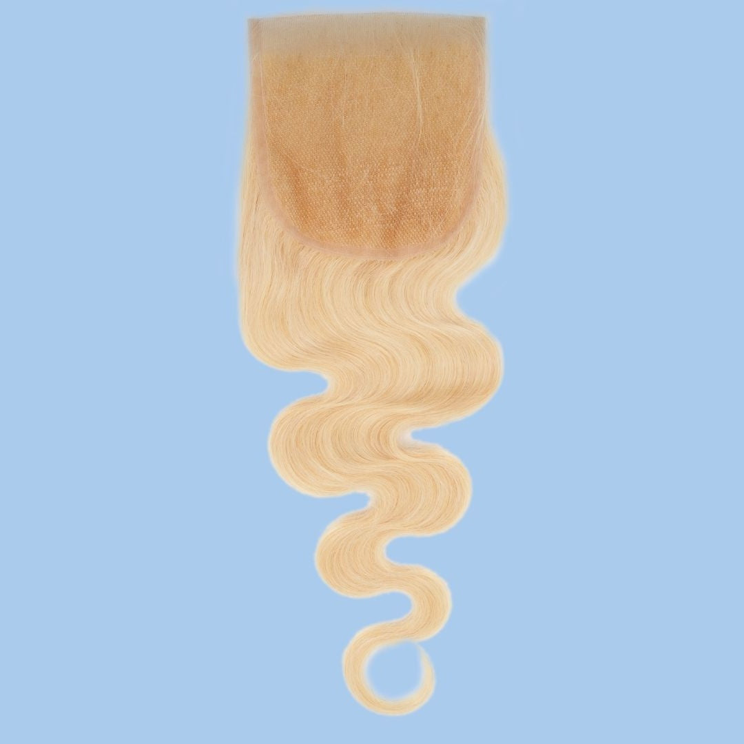 Transparent lace closure shown from the base with blonde body wave hair extensions hanging below, photographed on a blue backdrop