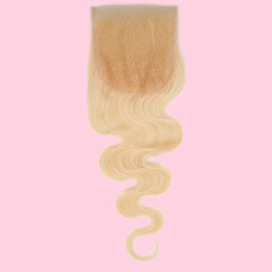 Transparent lace closure turned to show the lace base with blonde body wave hair extensions falling from it, on a pink backdrop