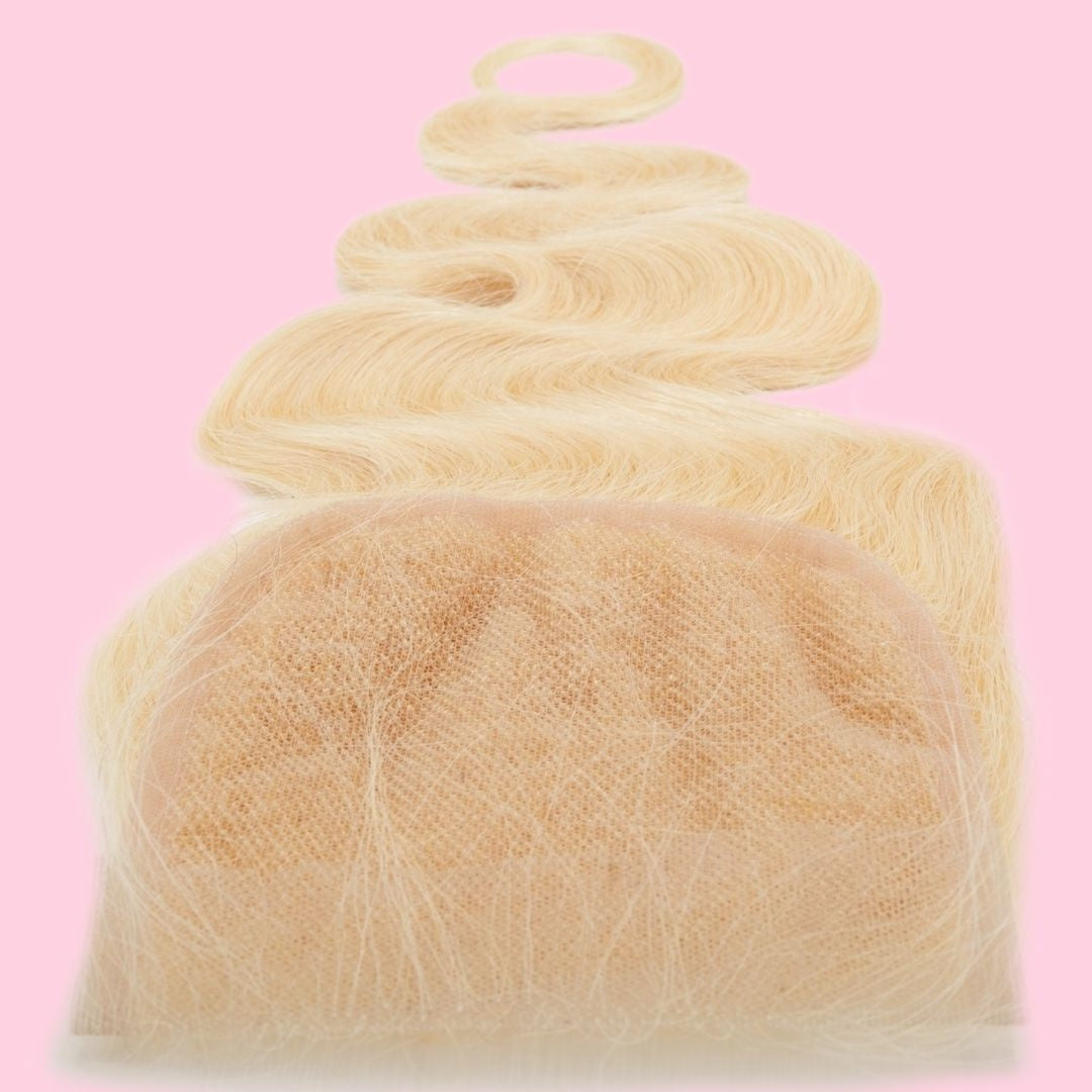 Close-up of the transparent lace panel and knots on a blonde body wave hair extensions closure against a pink backdrop