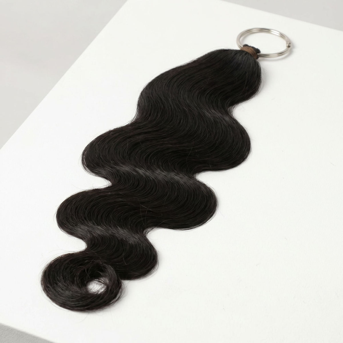 Natural black body wave crochet hank on its metal ring resting on a white block, showing the full wave of the hair extensions