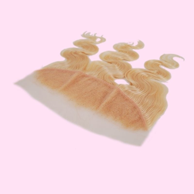 Blonde 613 body wave transparent frontal tilted on pink showing the lace base, the knotted roots and the waved lengths of the hair extensions