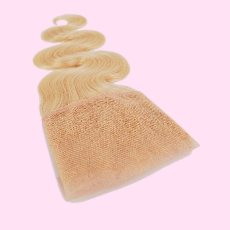 Angled view of the lace panel underside on a blonde 613 body wave transparent frontal with the waved hair extensions trailing behind on pink