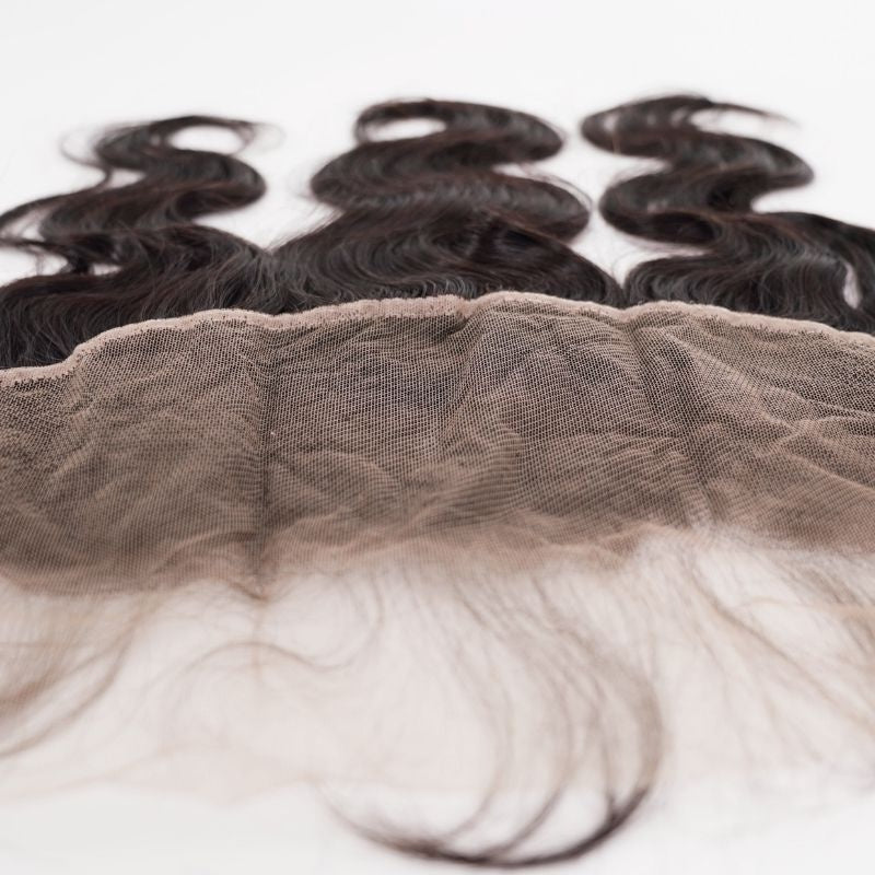 Detail of the lace mesh with fine baby hairs along its edge on the natural black body wave transparent frontal, waved hair extensions above