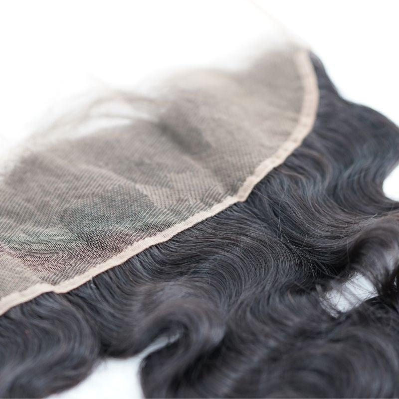 Close-up of the lace mesh and stitched edge of the natural black body wave transparent frontal with the waved hair extensions alongside