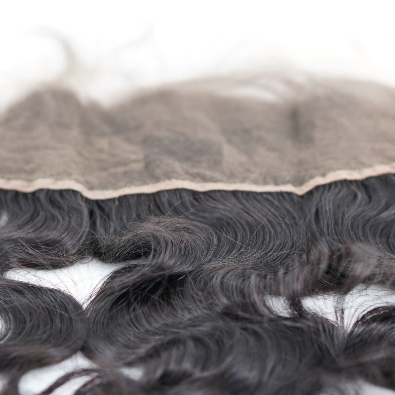 Underside close-up of the lace panel and its bound edge on the natural black body wave transparent frontal with waved hair extensions below