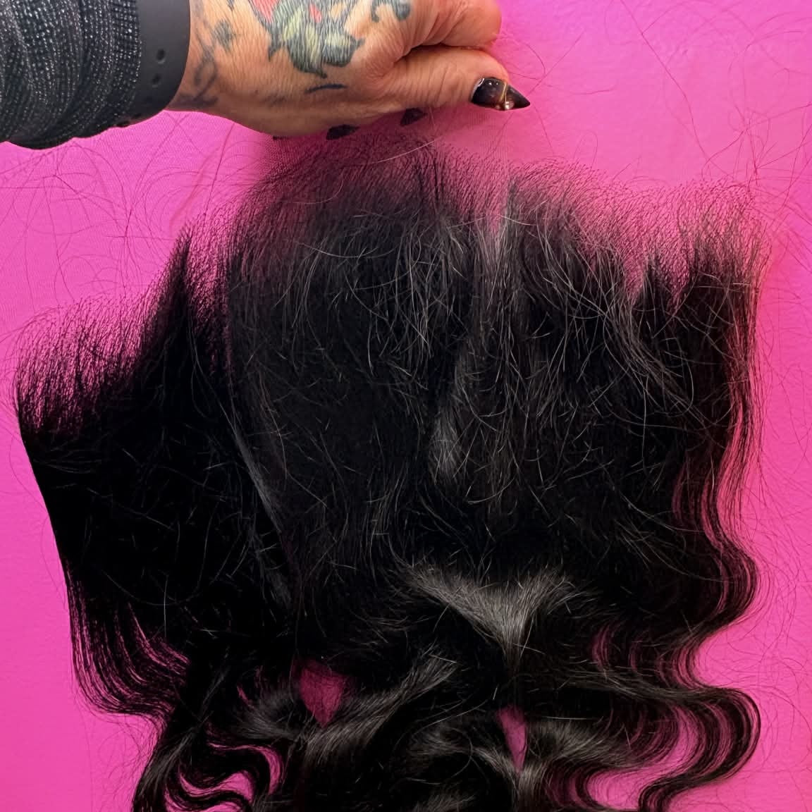 Hand holding 14 inch Brazilian body wave 13x6 HD lace frontal hair extension against pink wall showing S-wave texture and full hair length