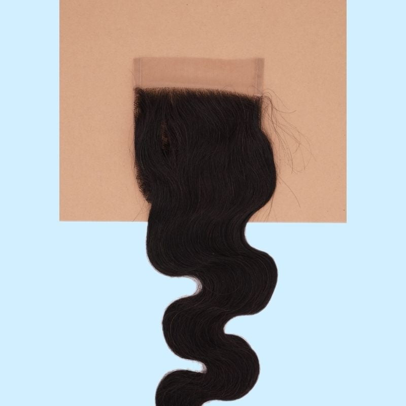 Natural black 4x4 transparent closure laid on a tan card over a blue background showing the lace top and the body wave hair extensions