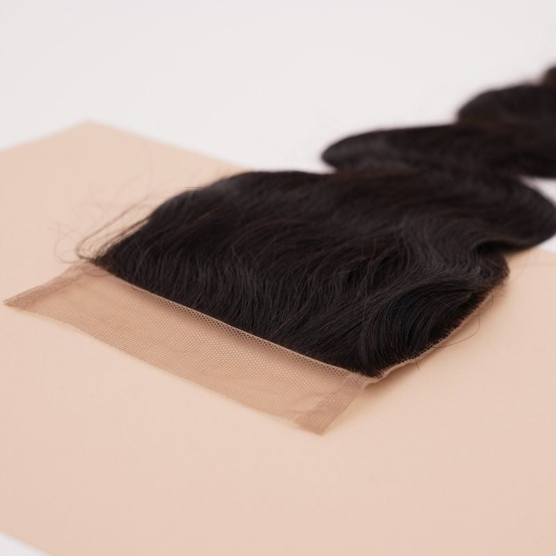 Natural black 4x4 transparent closure angled on a beige card so the lace edge and the roots of the body wave hair extensions show clearly