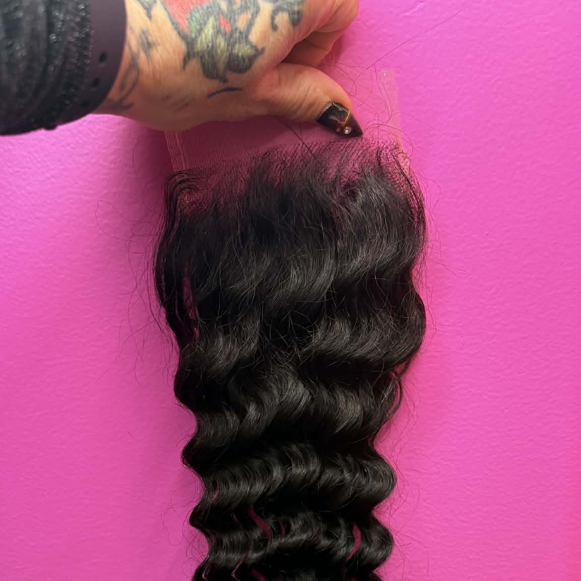 16 inch Brazilian deep wave 4x4 transparent closure hair extension held against pink background showing spiral curl definition and natural shine
