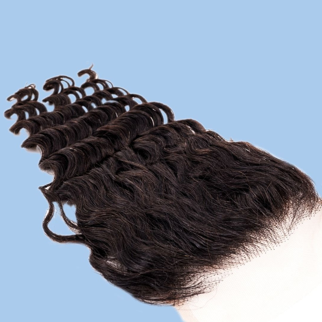 Natural black 4x4 transparent closure at an angle on a blue background with the lace panel at one end and deep wave hair extensions spread across the frame