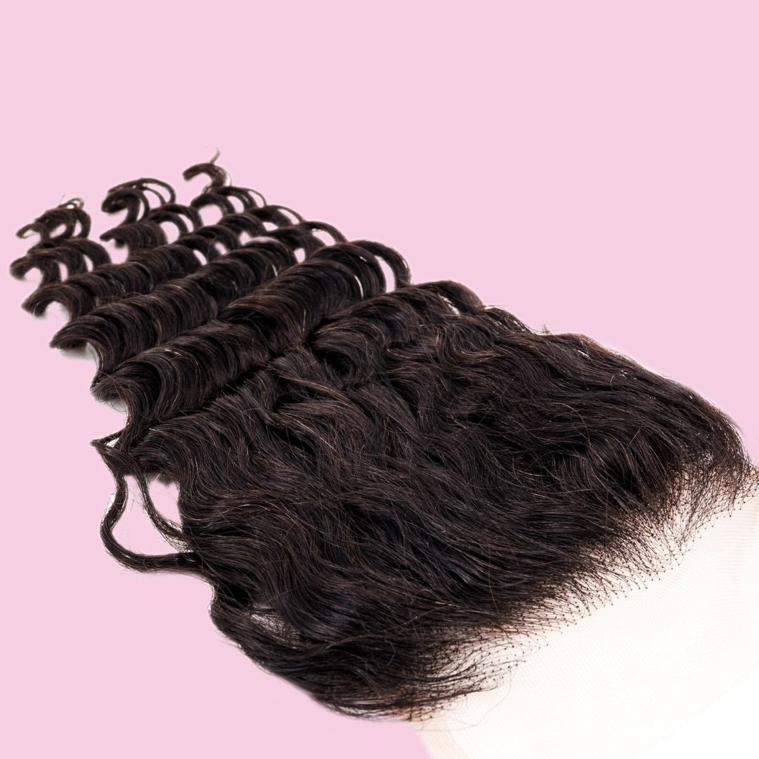 Natural black 4x4 transparent closure lying at an angle on pink with the lace panel at one end and the deep wave hair extensions spread out