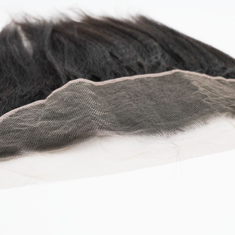 Angled close-up of the lace edge and knot line on a natural black kinky straight transparent frontal with the hair extensions lying behind