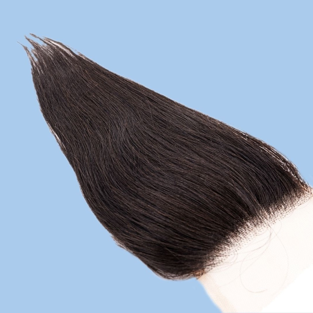 Angled crop on a blue background showing the lace corner of the closure and straight natural black hair extensions tapering to the ends