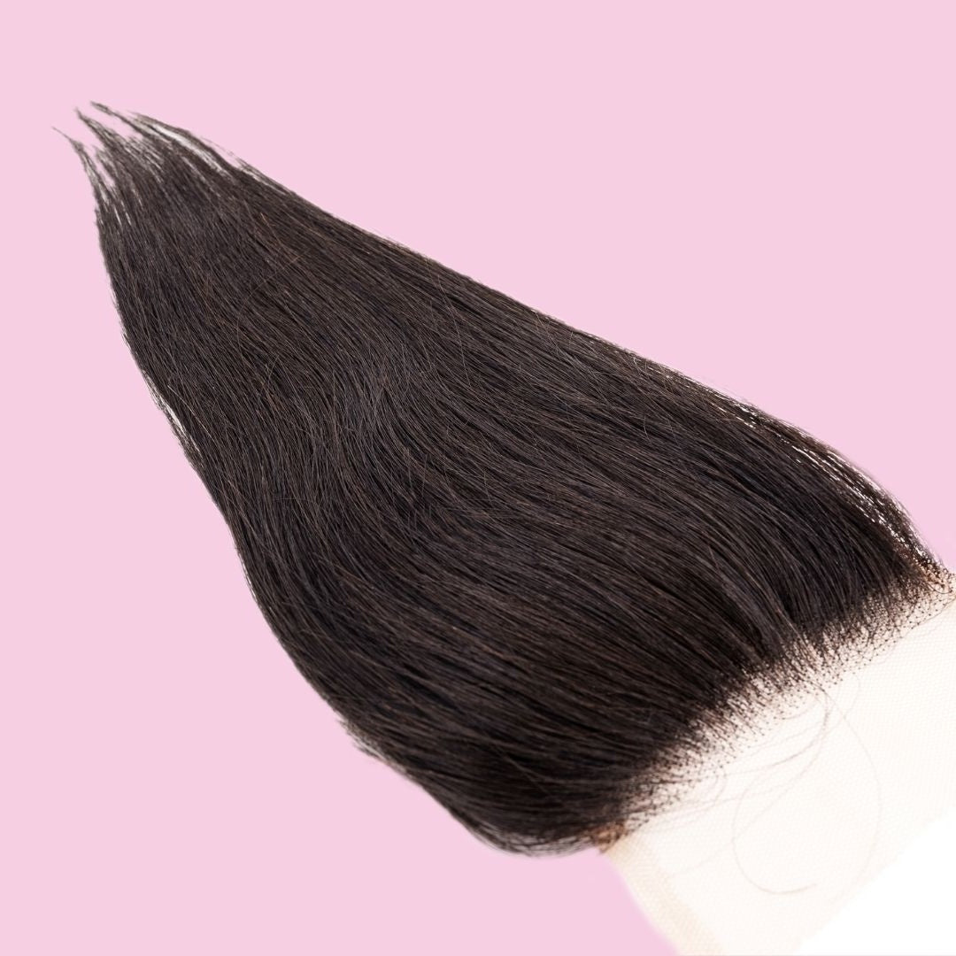 Angled crop on a pink background showing the lace corner of the closure and the smooth straight natural black hair extensions