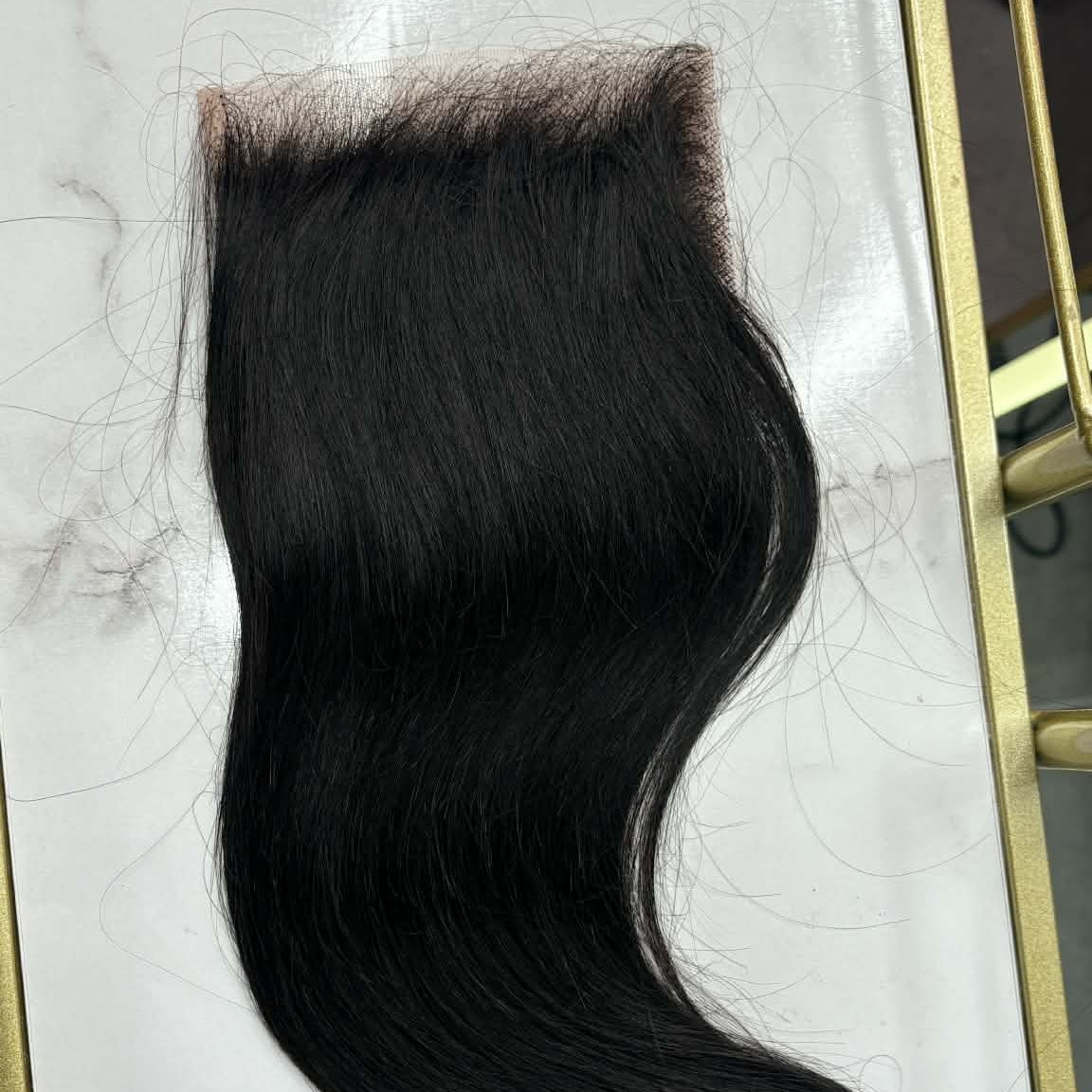 14 inch Brazilian straight 5x5 HD closure hair extension in gold frame on marble showing lace grid and straight hair flowing down