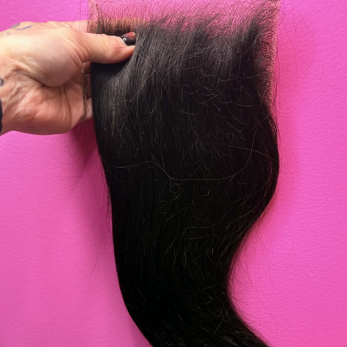Hand holding 14 inch Brazilian straight 5x5 HD closure hair extension against pink wall showing lace base and straight hair length