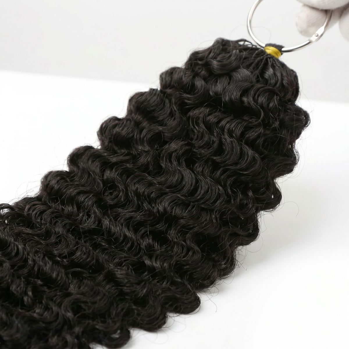Gloved hand holding the metal ring at the top of natural black curly crochet hair extensions with the curls hanging below