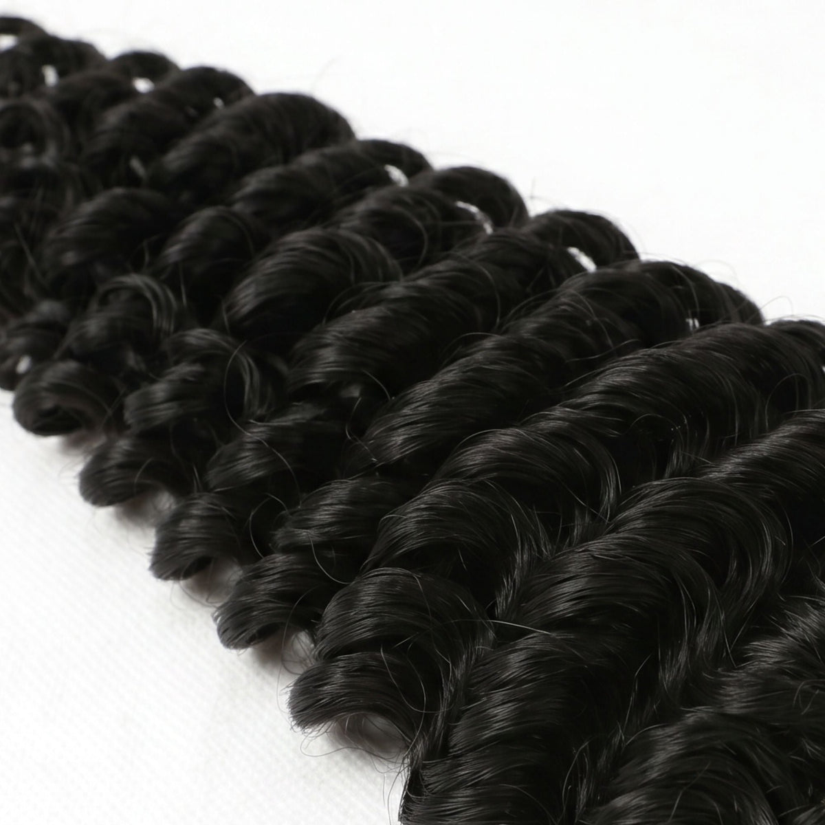 Close-up of the deep wave curl pattern on natural black feather crochet hair extensions laid on a white surface