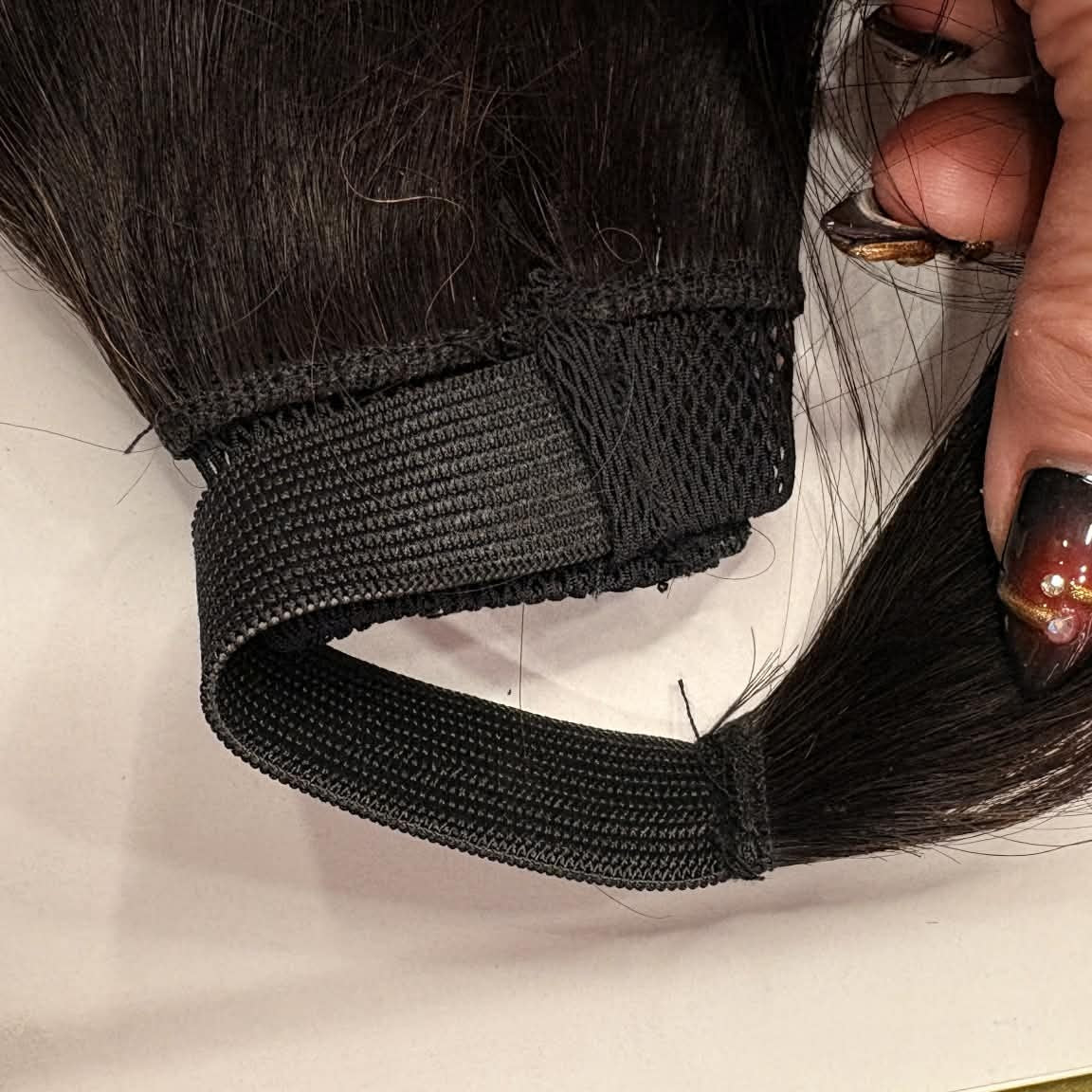 Close-up of drawstring ponytail mechanism held by hand showing wrap attachment and elastic band on 16 inch natural black ponytail hair extension