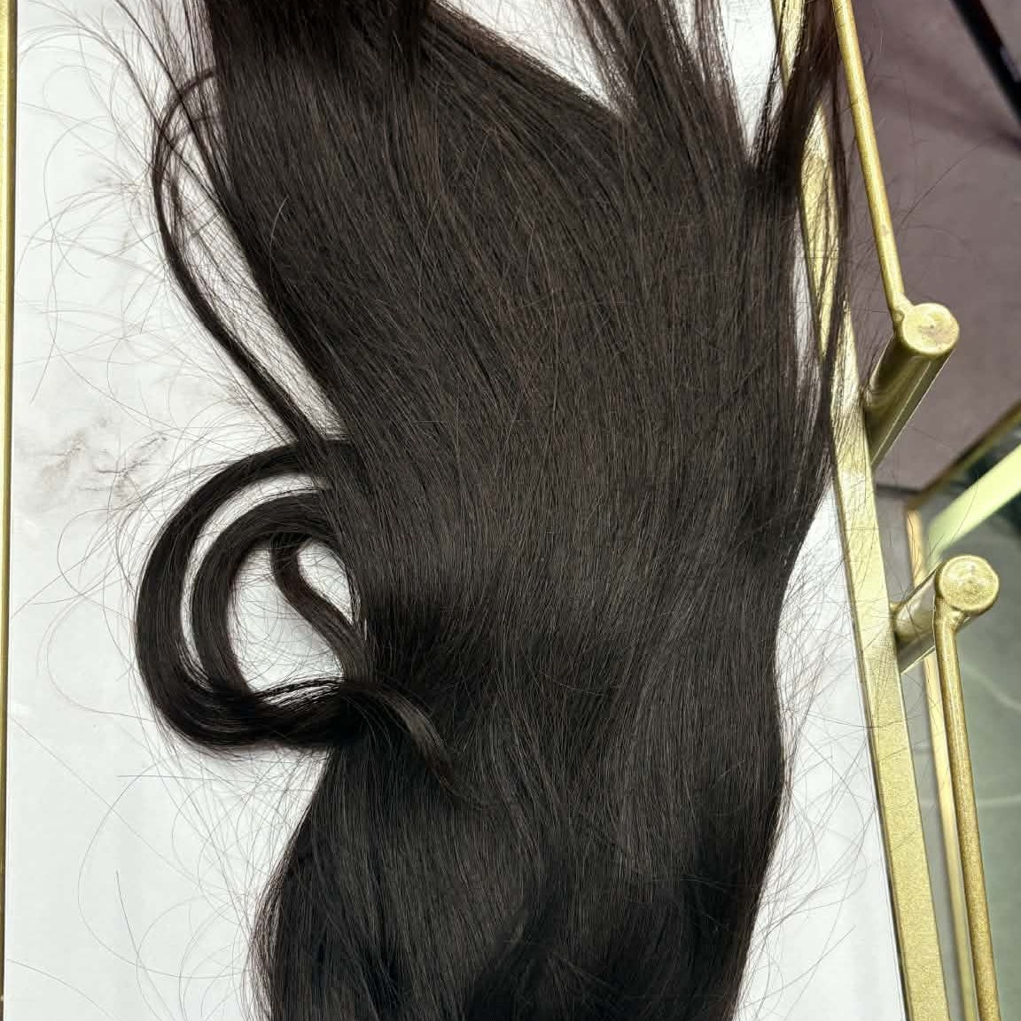 16 inch natural black ponytail hair extension laid flat on gold tray showing drawstring closure and full hair spread