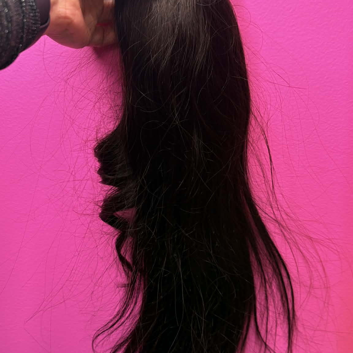 Hand holding 16 inch natural black ponytail hair extension against pink wall showing drawstring clip and full hair length