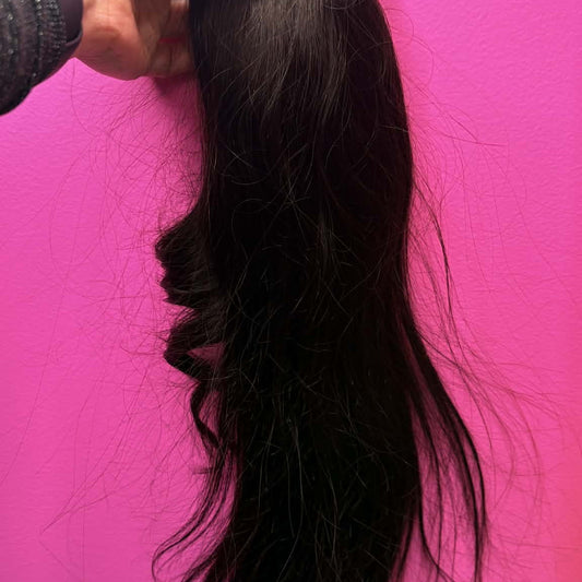 Hand holding 16 inch natural black ponytail hair extension against pink wall showing drawstring clip and full hair length