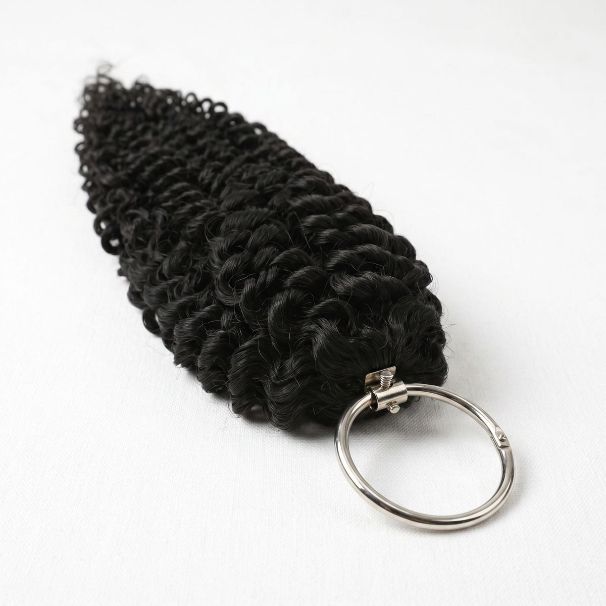 Hank of natural black water wave crochet hair extensions with the metal ring clasp at the bound end on a white surface