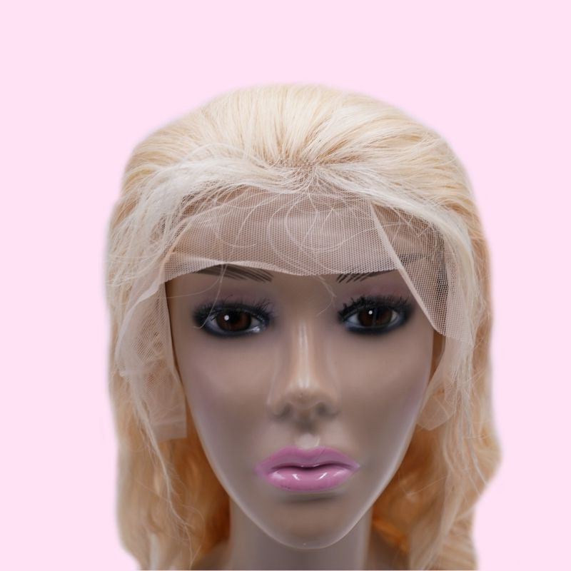 Front view of a blonde body wave human hair wig on a mannequin head against a pink backdrop with the transparent lace draped uncut
