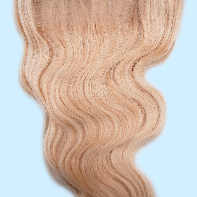Close-up of the wave pattern on a blonde body wave human hair wig against a pale blue background with the lace panel visible at the top