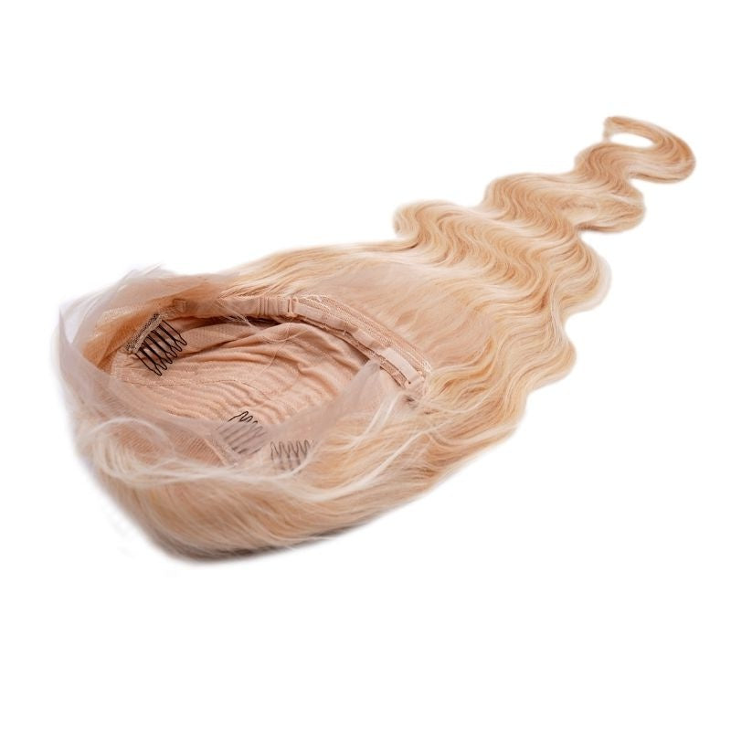 Blonde body wave human hair wig laid on its side on white showing the cap interior with combs and the waved hair trailing out