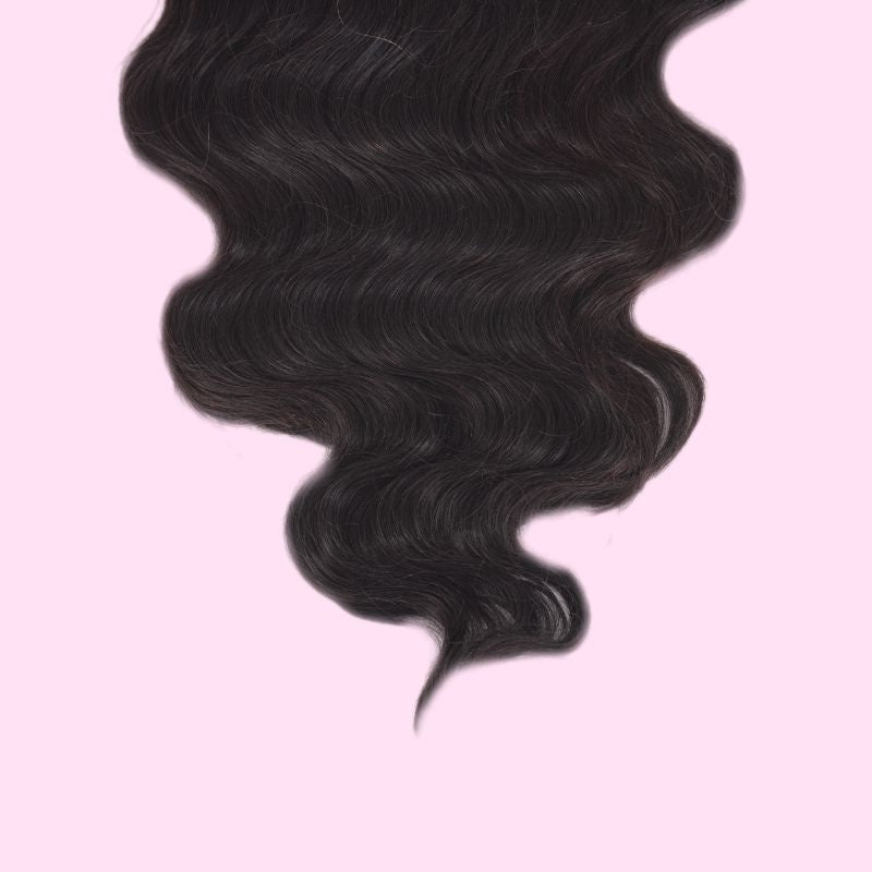 Detail of the ends on a body wave natural black human hair wig showing the S wave pattern against a pink background